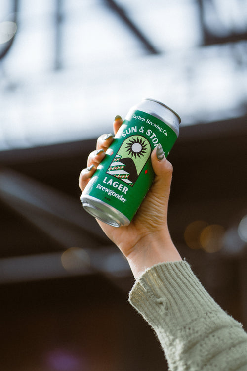 Hand holding a can of Sun & Stone Lager with a blurred background