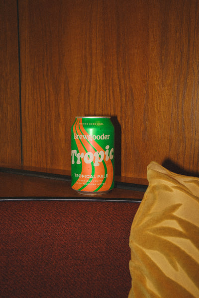Can of Brewgooder Tropic beer against a wood-panelled wall. Taken with a flash and edited in a 35mm style.